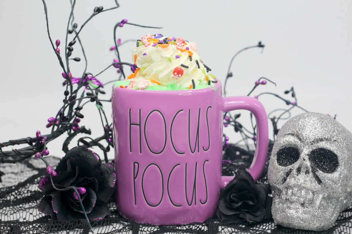 cup of whipped cream topped hot chocolate with halloween decor in the background